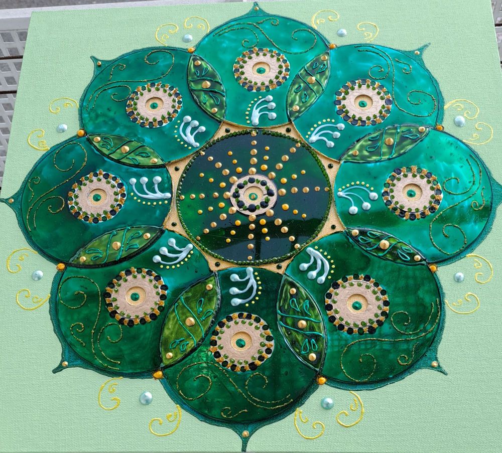 Canvas of a mandala made with recycled CDs, painted in emerald green, with details in forest green, gol, dark blue and turquoise. Background in pastel gree 
