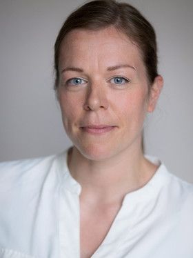 Headshot of woman in white shirt and blue eyes with hair in a low ponytail, smiling softly