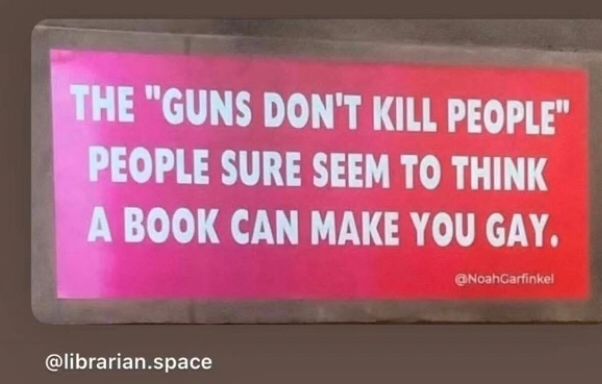 Sign that says The “ Guns don’t kill people” people sure seem to think a book can make you gay.