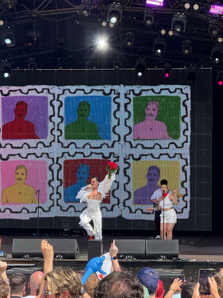 Pop Superstar Tom Aspaul wearing all white, performing a banger holding a bouquet of red flowers. 