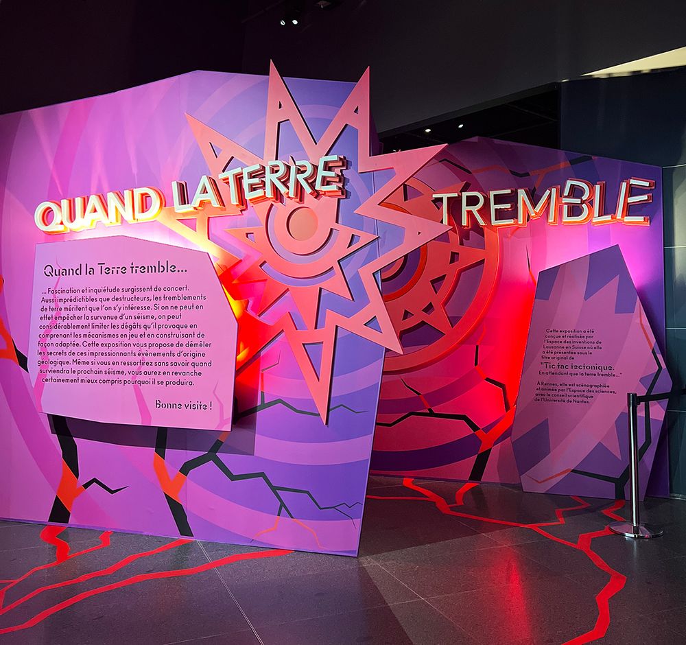Entrée de l'exposition "Quand la Terre tremble". Des stickers rouges, rappelant des fissures, ont été collé au sol. L'entrée de l'exposition est dans les tons rose/violet/rouge et la police d'écriture a un effet de tremblement.