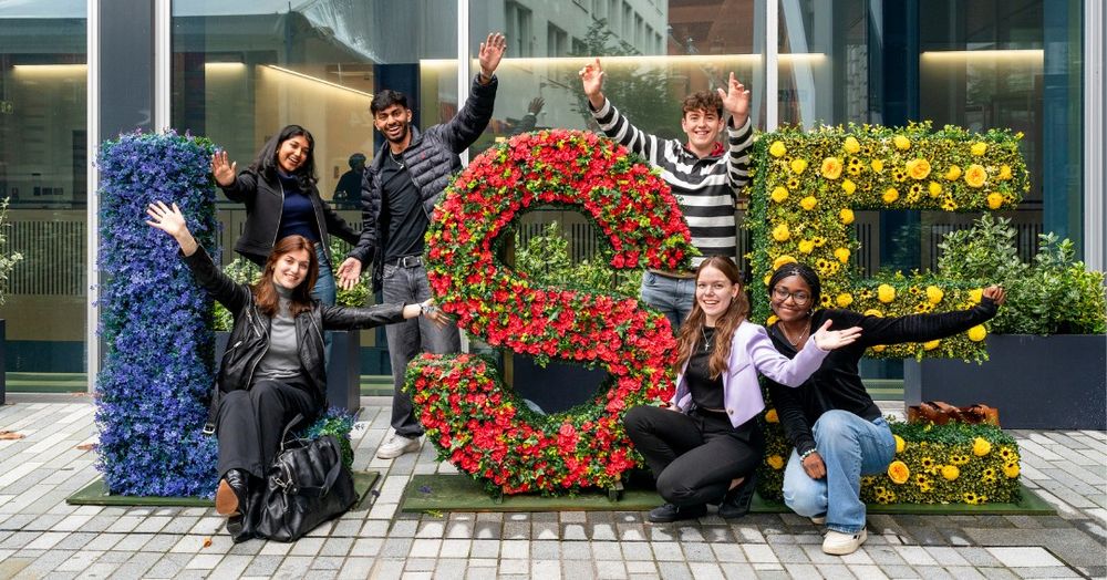 Six students by flower arrangement spelling out the letters LSE. 