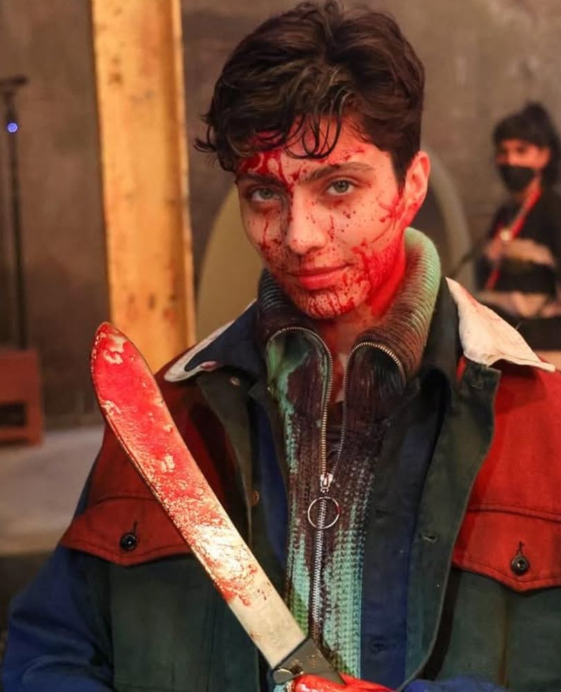 the wonderful xelia mendes-jones, covered in blood and holding a knoife. he is smiling up at the camera (we!!!!!!)