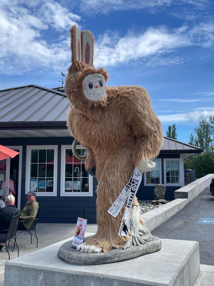 Sasquatch with a Labubu mask over its face, with big ears attached and fake oversize Pop Mart tags.