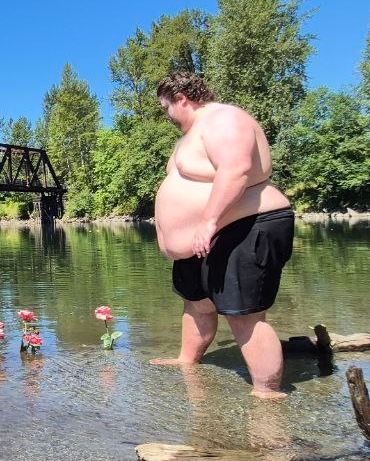 Ajchub obesely standing in the river next to some cut roses that were placed in the river bed
