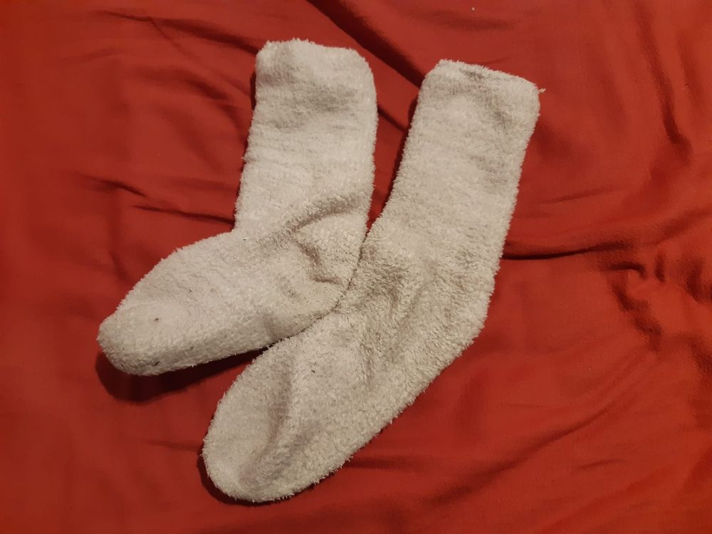 Foto weißer Kuschelsocken auf rotem, knittrigem Bettlaken.