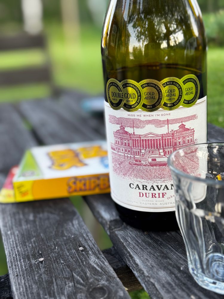 Ein Glas vor einer Flasche Rotwein vor einem Skip Bo Speil auf einem Holztisch in Schweden am See. 