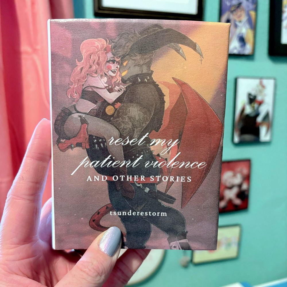 My hand holding a custom-bound book with an illustration by batkingsalem of Charlie and sinner!Adam looking at each other lovingly, with text that reads “reset my patient violent and other stories” and lists the author’s handle (me!) “tsunderestorm.”