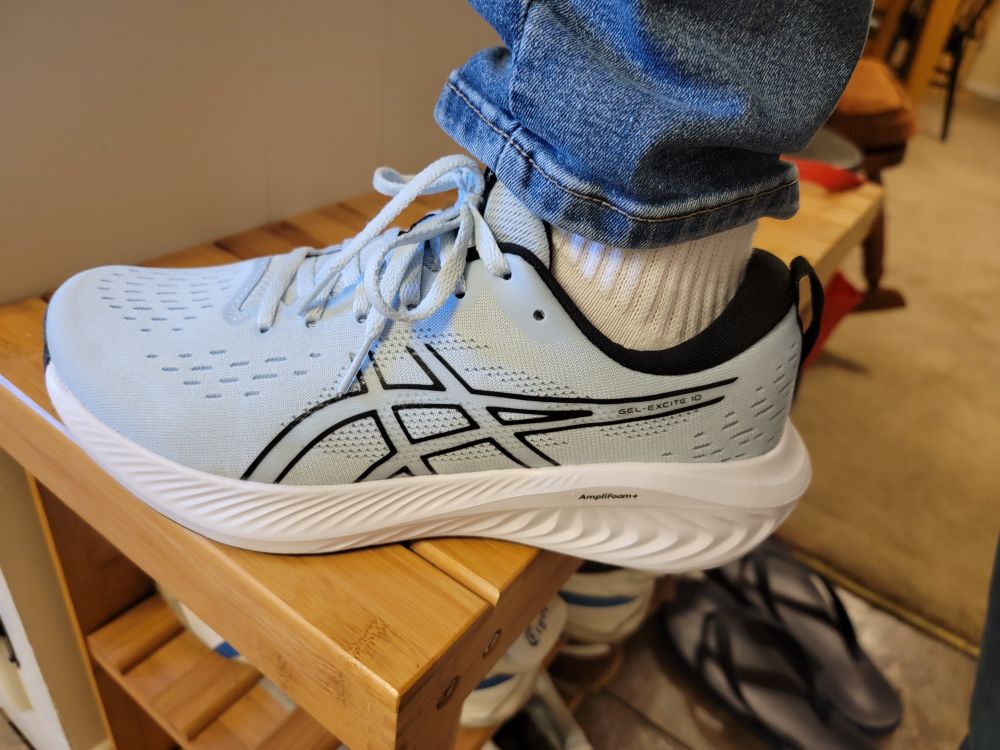 Close up of an Asics running shoe being worn.  It has a thick foam sole and is especially thick on the heel, as is the style lately.