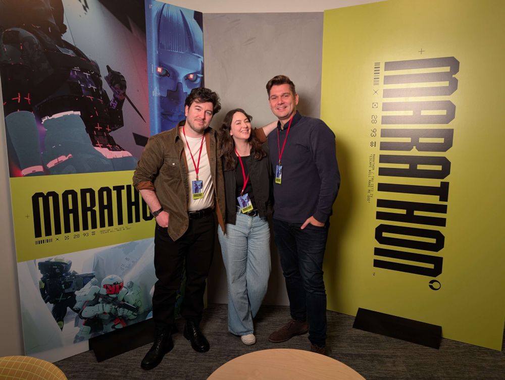 Jake, Lucy, and Ralph at Bungie in front of some Marathon branding 