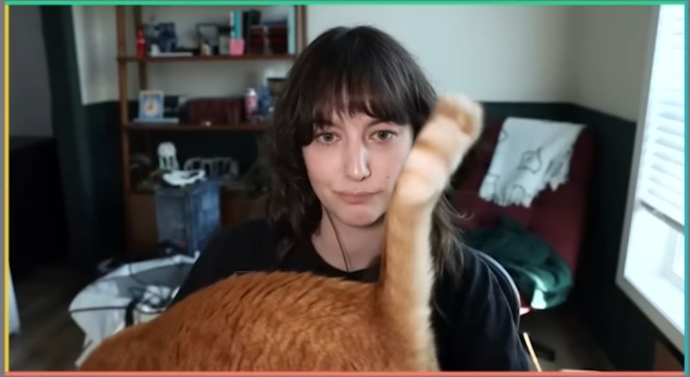 Screenshot of Lucy on the podcast but an orange cat has jumped up on the desk in front of her
