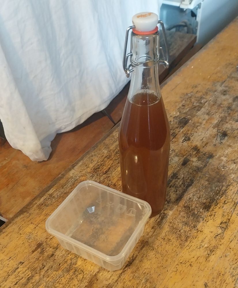 Bouteille d1/2 litre de cidre et boîte en plastique alimentaire posées sur un meuble de cuisine en bois clair. 