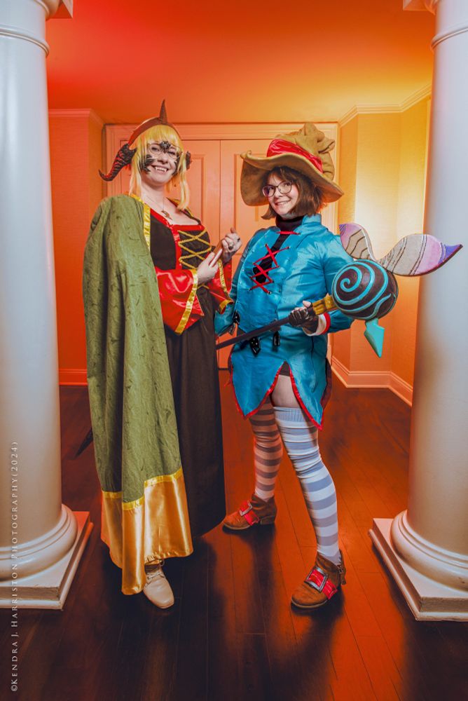 Cosplay photo two characters standing side by side, between two white pillars. Left character is a female Au'Ra Summoner from Final Fantasy XIV. On the right is a female Black Mage from Final Fantasy: Crystal Chronicles. 