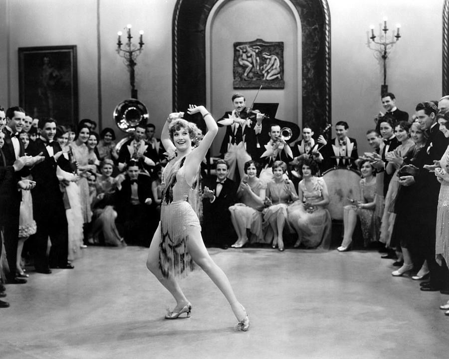 A young Joan Crawford dancing in a ballroom as onlookers clap.