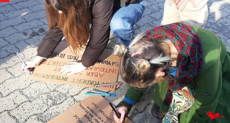 Zwei junge Frauen knien auf dem Boden und schreiben Plakate.