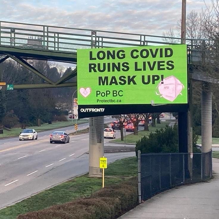 Next to a busy street, a neon green billboard reads, Long Covid ruins lives. Mask up. There is an image of an N95 mask and the heart shaped PoP BC logo.