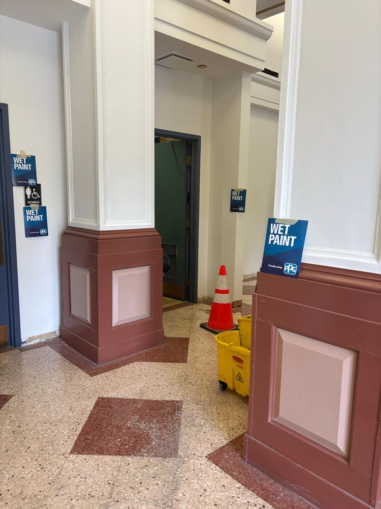 A series of four signs that all read “wet paint” around a set of freshly painted columns 