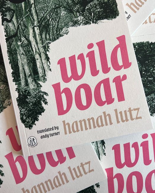 Copies of Wild Boar stacked on top of one another. The cover is cream with a green, illustrated forrest and pink text. 