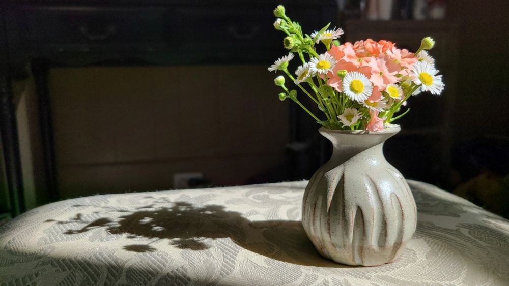 Light gray bud vase of orange and yellow flowers in the sun. (Some are tiny adorable daisies)