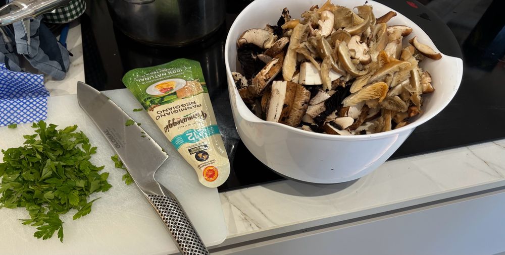Mushrooms, parsley, parmesan & sharp knife on a worktop. 