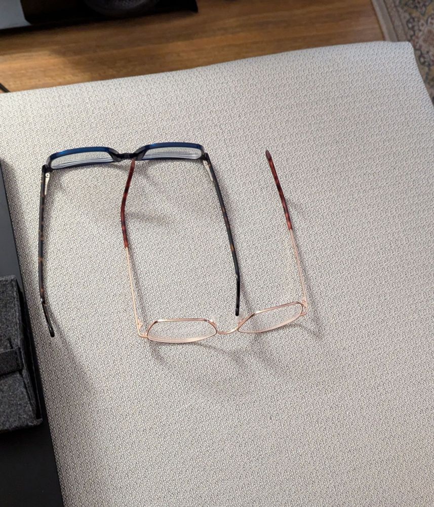 Two pairs of glasses lying next to each other on a sofa.