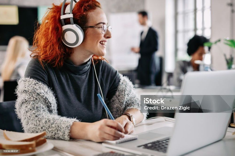 Student wearing headphones, taking notes and working on a laptop.