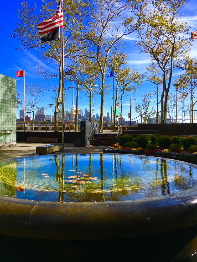 Vietnam Veterans Memorial NYC A US flag flies over a reflective pool surrounded by trees and walls of names 
