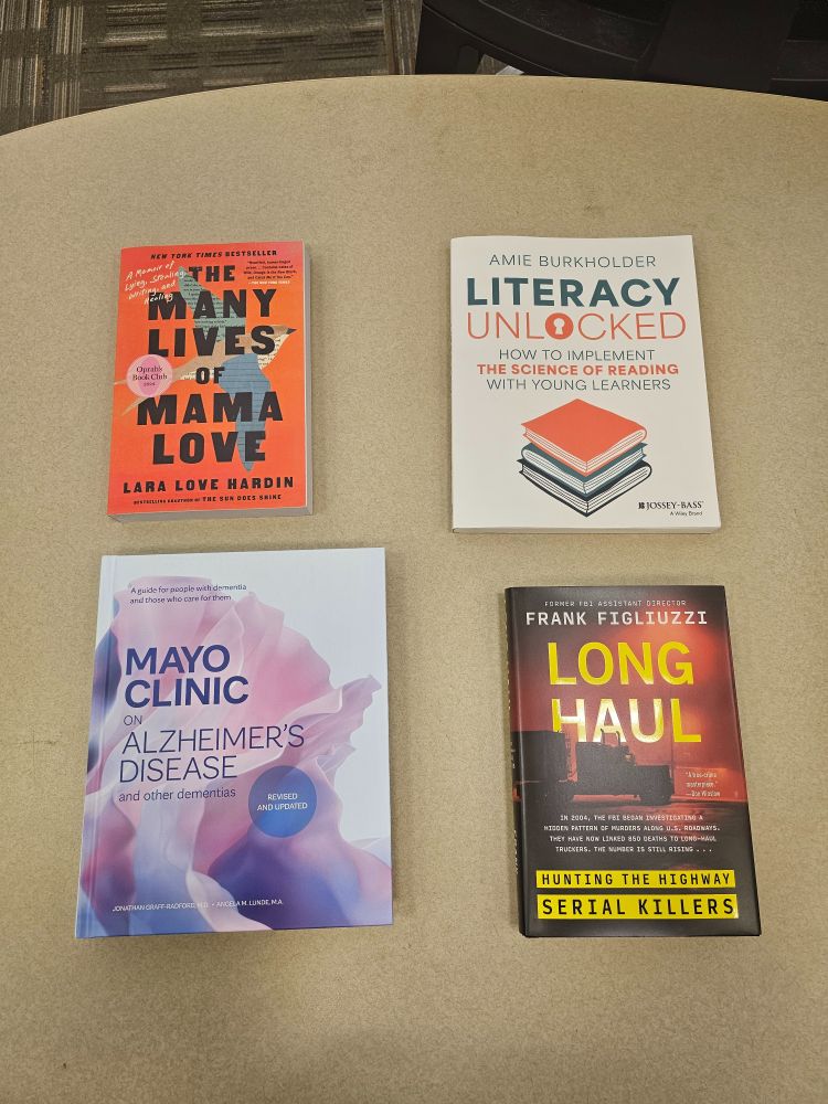 Four nonfiction books on a table, clockwise from top left: The Many Lives of Mama Love by Lara Love Hardin, Literacy Unlocked by Amie Burkholder, Long Haul: Hunting the Highway Serial Killers by Frank Figliuzzi, and Mayo Clinic on Alzheimer's Disease and Other Dementias.