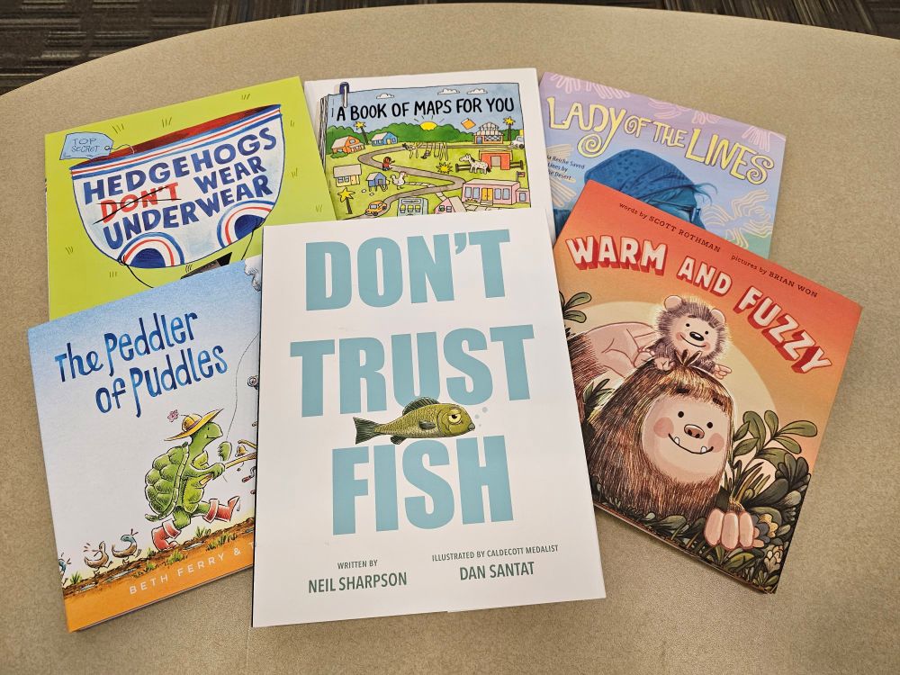 Six books spread on a table:
Hedgehogs Don't Wear Underwear by Marisa Valdez
A Book of Maps for You by Lourders Heuer with Maxwell Eaton III
Lady of the Lines by Michaela MacColl
The Peddler of Puddles by Beth Ferry & Tom Lichtenheld
Don't Trust Fish by Neil Sharpson with Dan Santat 
Warm and Fuzzy by Scott Rothman with Brian Won