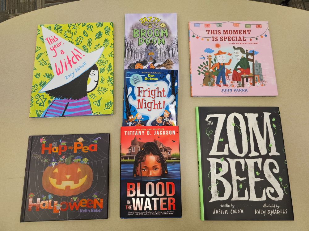 Spooky season kids books! Top left is This Year A Witch by Zoey Abbott, lower left is Hap-pea Halloween by Keith Baker, center top to bottom are Jazzy the Witch in Broom Doom, Fright Night by Dan Gutman, Blood in the Water by Tiffany D. Jackson, then top right is This Moment is Special by John Parra, and lower right is Zom-bees by Justin Colon with Kay Quarles. 