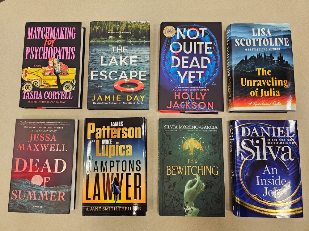 Eight fiction books on a table, left to right from top left: Matchmaking for Psychopaths by Tasha Coryell, The Lake Escape by Jamie Day, Not Quite Dead Yet by Holly Jackson, The Unraveling of Julia by Lisa Scottoline, Dead of Summer by Jessa Maxwell, Hampton's Lawyer by James Patterson and Mike Lupica, The Bewitching by Silvia Moreno-Garcia, and An Inside Job by Daniel Silva.