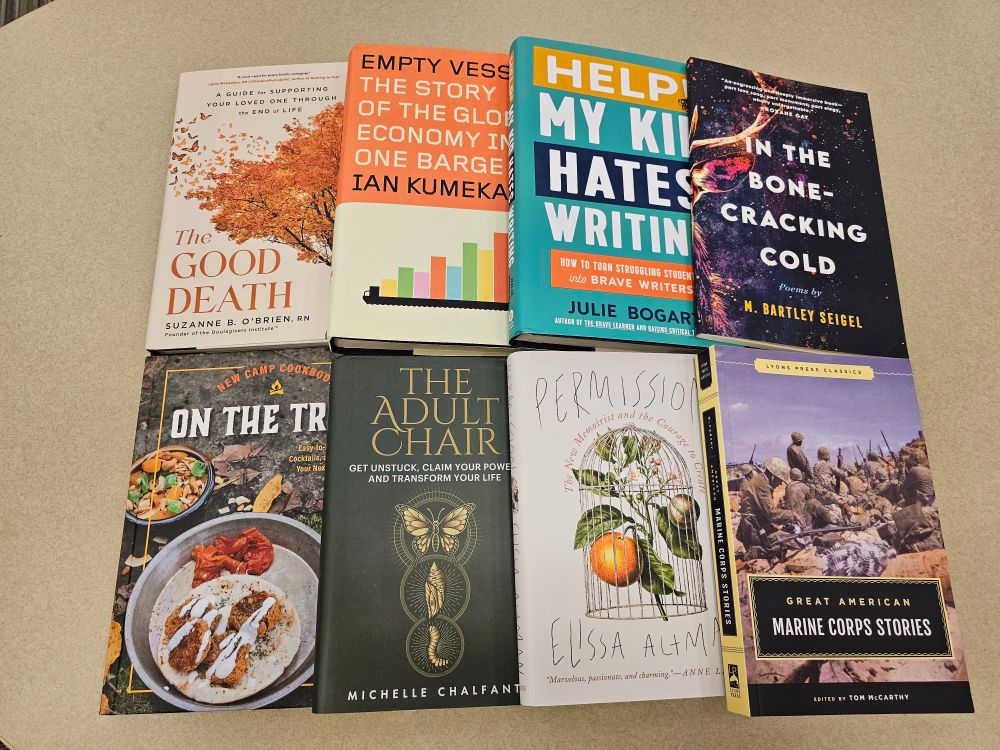 Eight books spread on a table, from top left: The Good Death by Suzanne B. O'Brien, RN, Empty Vessel by Ian Kumekawa, Help! My Kid Hates Writing by Julie Bogart, In the Bone-Cracking Cold by M. Bartley Seigel, New Camp Cookbook On the Trail by Emily Vikre, The Adult Chair by Michelle Chalfant, Permission by Elissa Altman, and Great American Marine Corps Stories edited by Tom McCarthy.