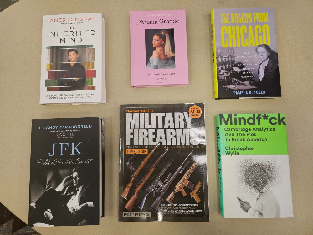 Six nonfiction books on a table, from top left: The Inherited Mind by James Longman, Icons of Style: Ariana Grande by Caroline Young, The Dragon from Chicago by Pamela D. Toler, J.F.K. Public Private Secret by J. Randy Taraborreli, The Standard Catalog of Military Firearms, and Mindf*ck: Cambridge Analytica and the Plot to Break America by Christopher Wylie