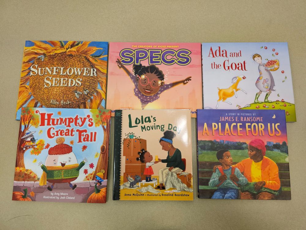 Six kids books on a table, from top left: Sunflower Seeds by Ellen Heck, Specs by Van G. Garrett with Reggie Brown, Ada and the Goat by Heidi Aubrey, Humpty's Great Fall by Amy Moore with Josh Cleland, Lola's Moving Day by Anna McQuinn with Rosalind Beardshaw, and A Place for Us by James E. Ransome.