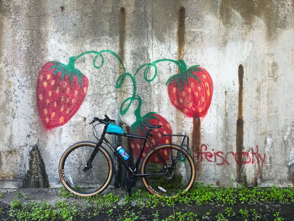 A black bike leaning against a wall with strawberries painted on it 