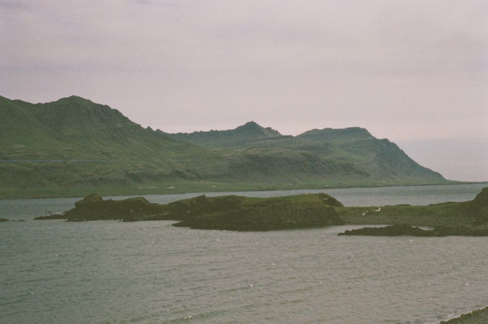 Grey seawater in a small bay, surrounded by rocky hills. A spit of land cuts the bay in half.