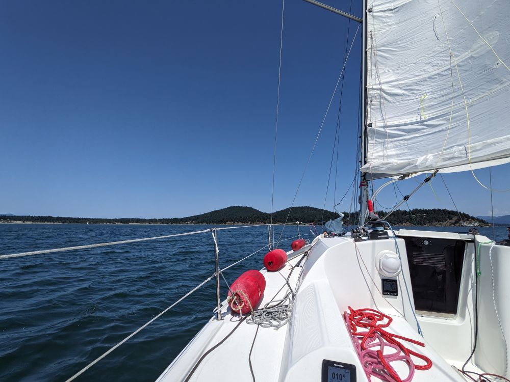 a sailboat on a dark blue sea under main heading towards a tree covered island 