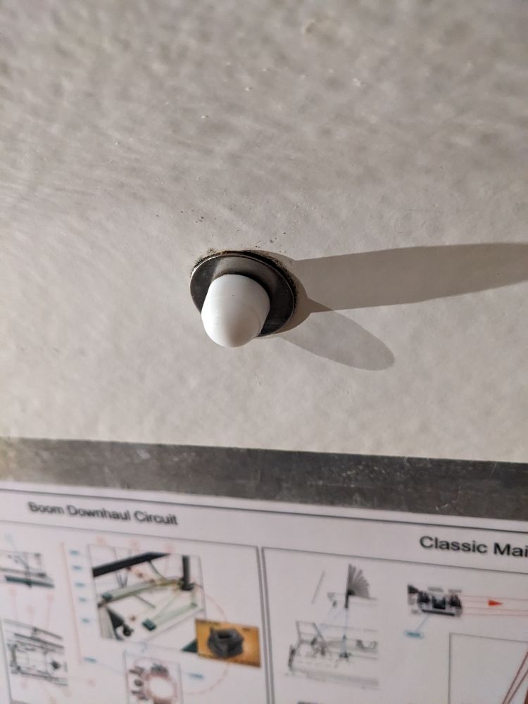 A white nut cap on the fiber wall/ceiling of a sailboat. 
