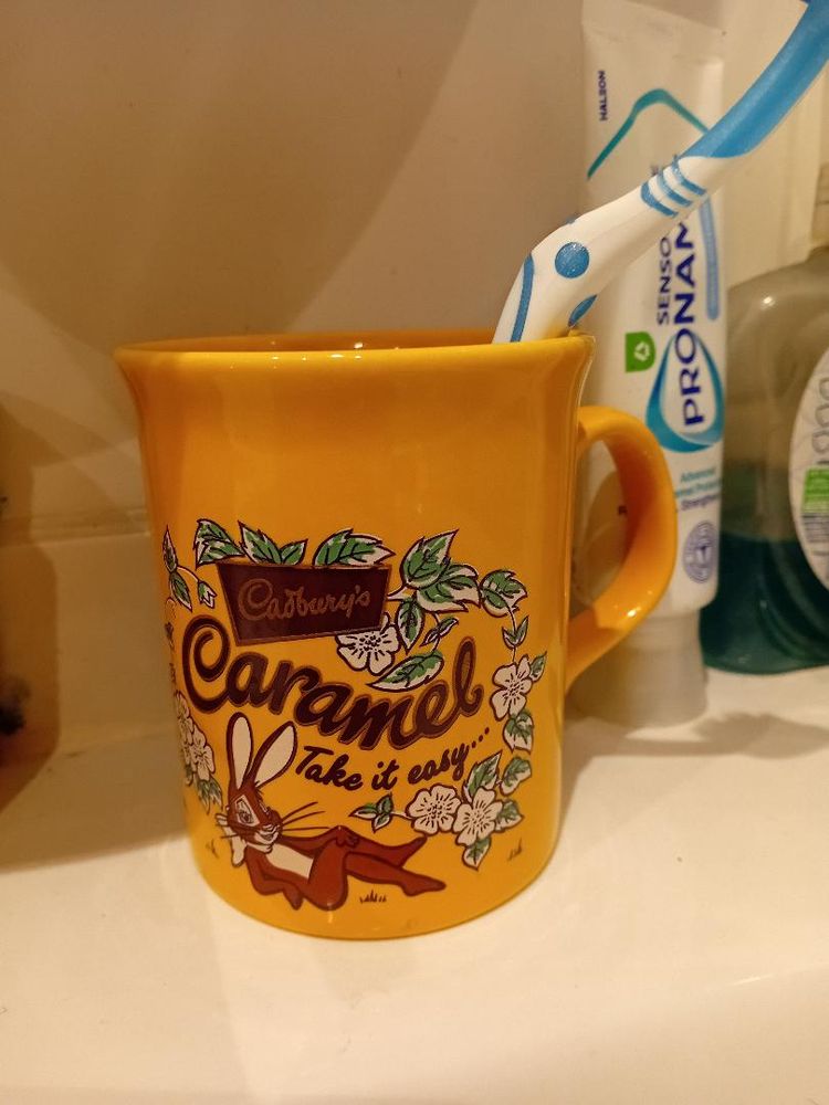 a yellow mug being used as a toothbrush holder, decorated with an image of the Cadbury Caramel Bunny.