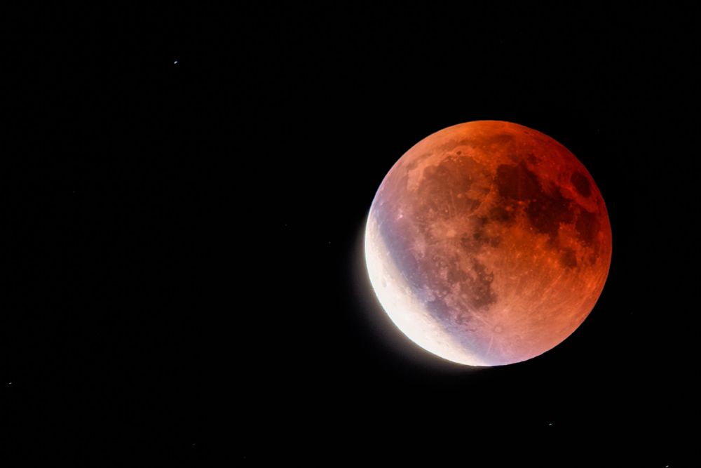 Red colored moon shortly after eclipse with small portion really bright.