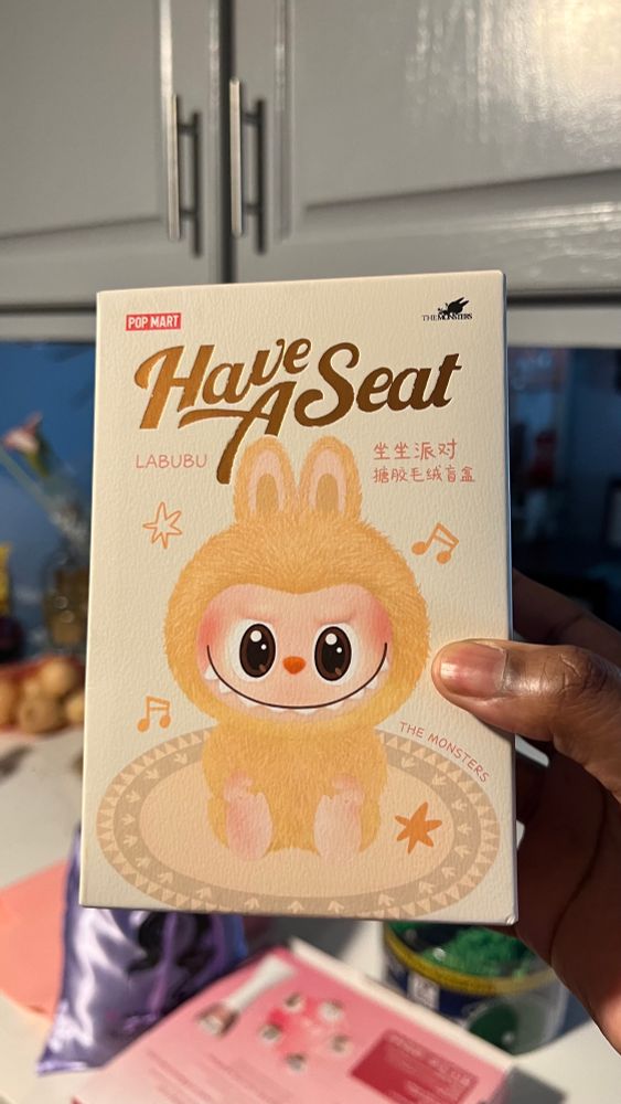 a photo of raynna holding a “have a seat” labubu box