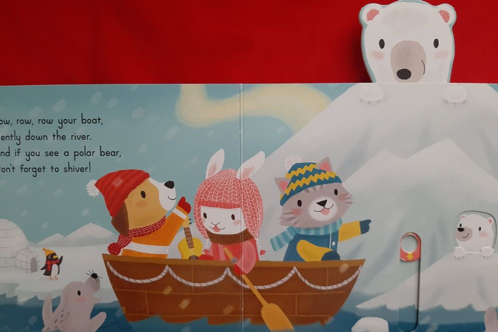 Page from a children's book called 'row row your boat', showing a polar bear and penguin living on ice, while a cat, dog and rabbit dressed in clothes go past in a row boat. Text is 'row row row your boat gently down the river, if you see a Polar bear don't forget to shiver'. 