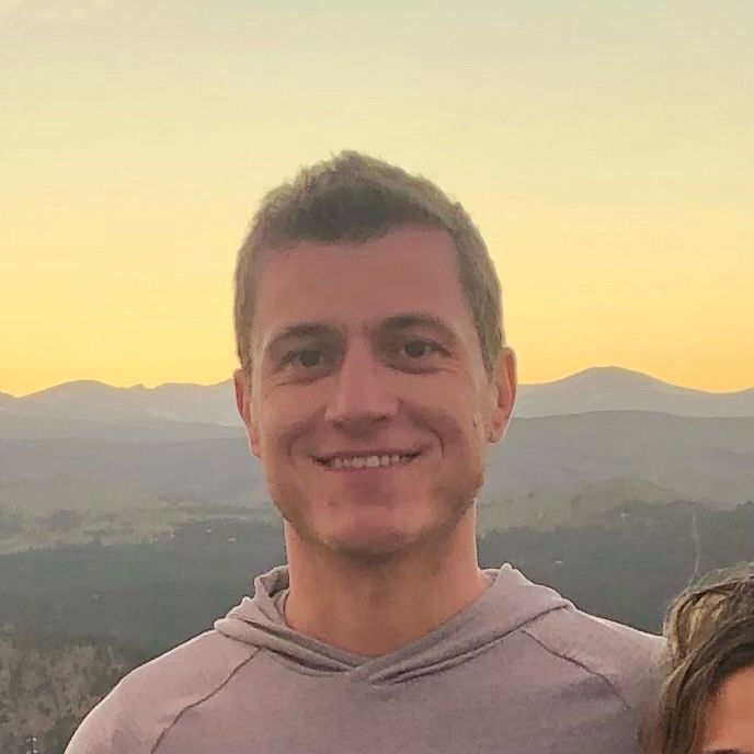 A photo of me, a white man in his mid thirties, smiling with a mountain sunset in the background.