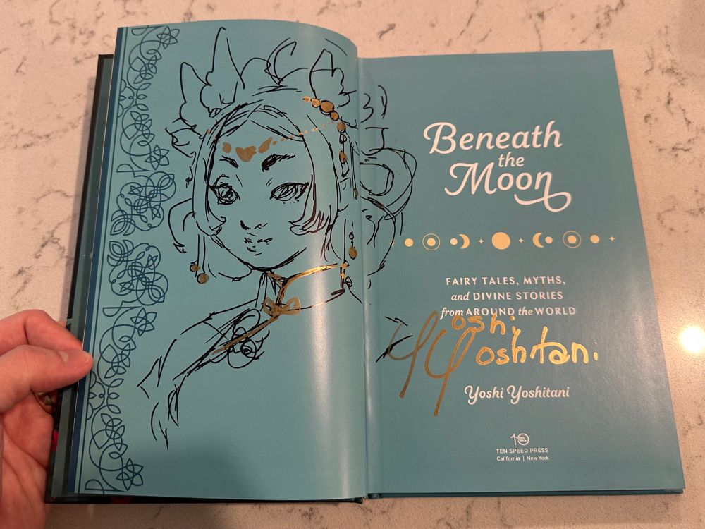 The inside cover page of Yoshi Yoshitani’s book, “Beneath the Moon: FAIRY TALES, MYTHS, and DIVINE STORIES from AROUND the WORLD” There is a doodle of a woman in black and gold ink and Yoshi’s signature.
