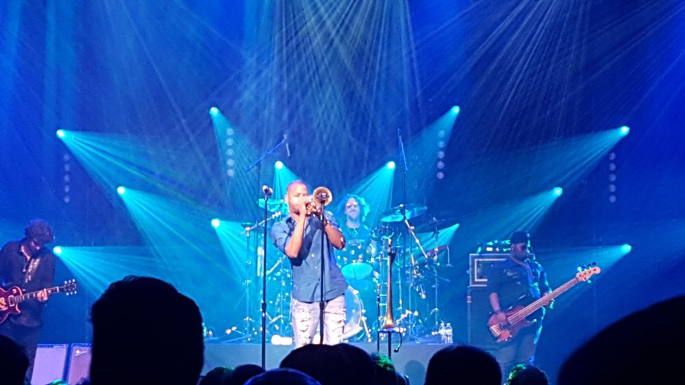 Trombone Shorty on stage at The Palace playing trumpet, also showing guitarist, bassist, and drummer.