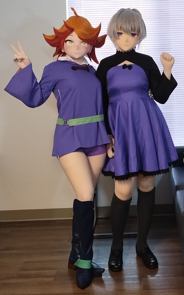 Two kigurumi cosplayers posing side by side. The one on the left is Amanda O'Neill from Little Witch Academia, wearing her flight uniform, and posing with a peace sign. The one on the right is Yin from Darker Than Black, wearing her usual purple dress and posing with a raised hand.