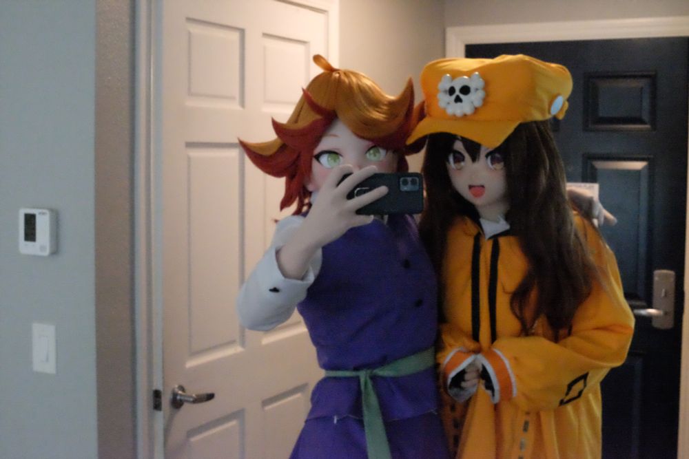 The same two kigurumis taking the selfie, but now the photo is being taken from further away by a second camera.