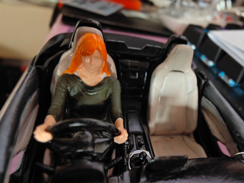 Model of a woman with orange hair sitting in a car, holding the steering wheel