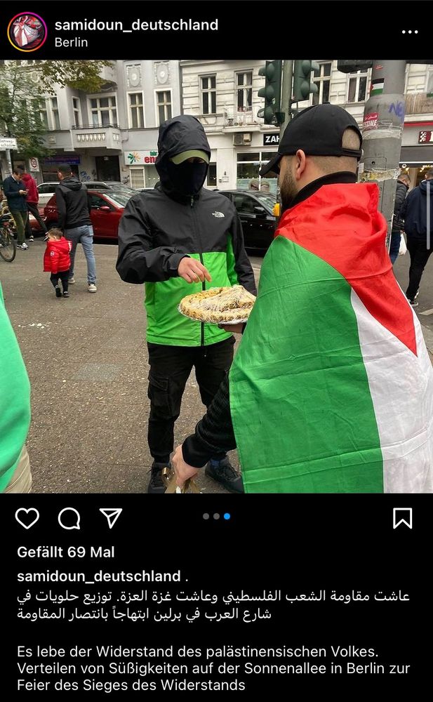 Ein Screenshot von Samidoun Deutschland. Ein Mann in palästinensischer Fahne verteilt Süßigkeiten. Darunter steht auf arabisch und deutsch: „Es lebe der Widerstand des palästinensischen Volkes. Verteilen von Süßigkeiten auf der Sonnenallee in Berlin zur Feier des Sieges des Widerstands.