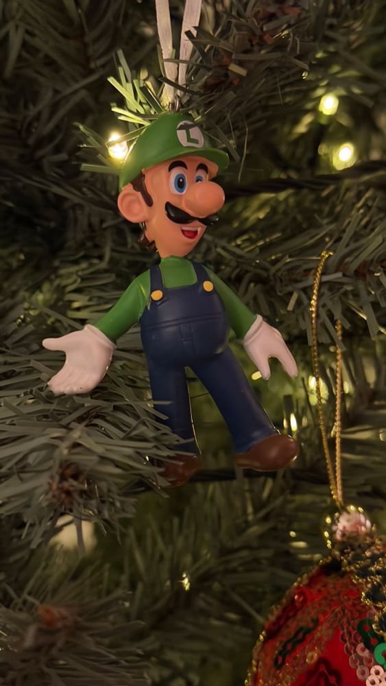 Photograph of a Christmas tree ornament of Luigi from Super Mario Bros. hanging in a Christmas tree
